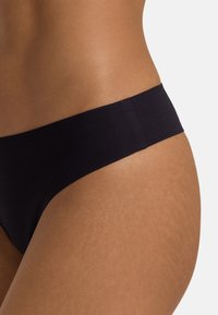 Schwarze Bikini-Hose mit einer glatten, weichen Textur, die einen nahtlosen Bund und ein minimalistisches Design aufweist. Die Seitenansicht hebt die Kurven hervor.