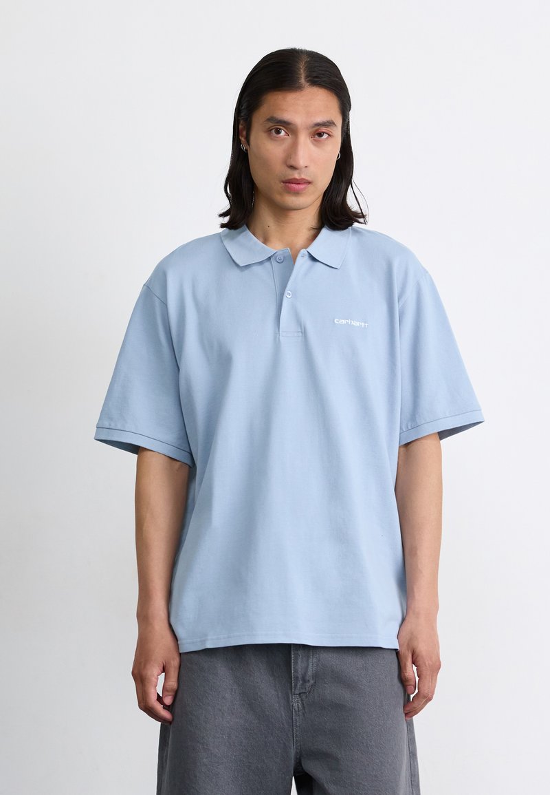 Polo bleu clair avec des manches courtes et oversized, doté d'un col, affichant un petit logo blanc sur la poitrine gauche. Matière en coton doux.