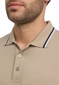 Beige poloshirt van textuurstof, voorzien van een twee-knopen placket en een kraag met marineblauwe en witte gestreepte accenten.