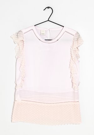 Blusa sin mangas de color rosa claro con mangas y dobladillo de malla transparente con puntos y volantes, colgada en una percha de alambre negra sobre un fondo blanco.