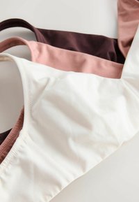 Trīs krūšturi dažādās krāsās: tumši brūna, maigi rozā un off-white. Tie ir izgatavoti no mīksta auduma, ar bezšuvju dizainu un plānām siksnām.