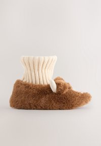 Chausson marron duveteux ressemblant à un ours, avec un bord-côtes en tricot crème et un petit détail d'oreille tricotée sur le côté.