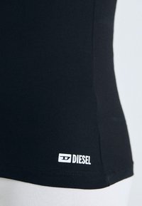 Juodas prigludęs tank topas, pagamintas iš lygaus audinio, su nedideliu baltu "DIESEL" logotipu apatiniame dešiniajame kampe.