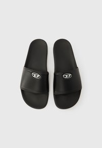 Sorte slidssandaler med glat syntetisk materiale, bred rem og et sølvfarvet logo-detalje på oversiden. Flad, tekstureret ydersål.