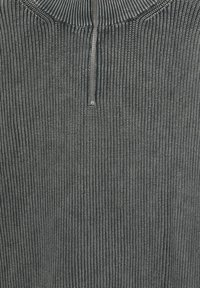 Pulover cărbune cu model în relief, cu guler înalt și fermoar până la jumătate. Texturea pare moale și tricotată, arătând o cusătură uniformă și constantă.