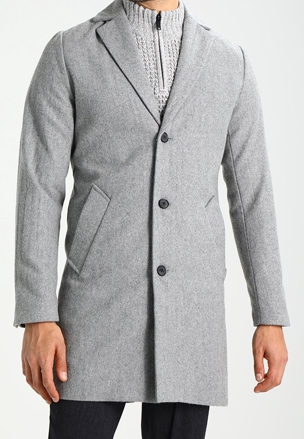 Manteau en laine gris avec col cranté, fermeture boutonnée, poches latérales et coupe ajustée. Porté par-dessus un pull en maille texturée.