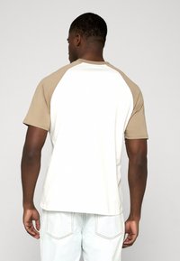 T-shirt à manches courtes avec un corps blanc et des manches raglan beige, confectionné dans un tissu doux. Comprend un col arrondi et une coupe décontractée.