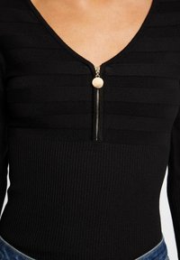 Svart ribbad bodysuit med V-ringning och främre dragkedjestängning, med horisontella ränder och detaljer i guldton.