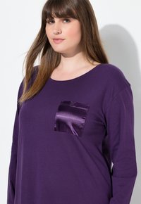 Lila långärmad topp i bomull med en glänsande satinlapp. Har en vid halsringning och en avslappnad passform. Slät textur över hela plagget.