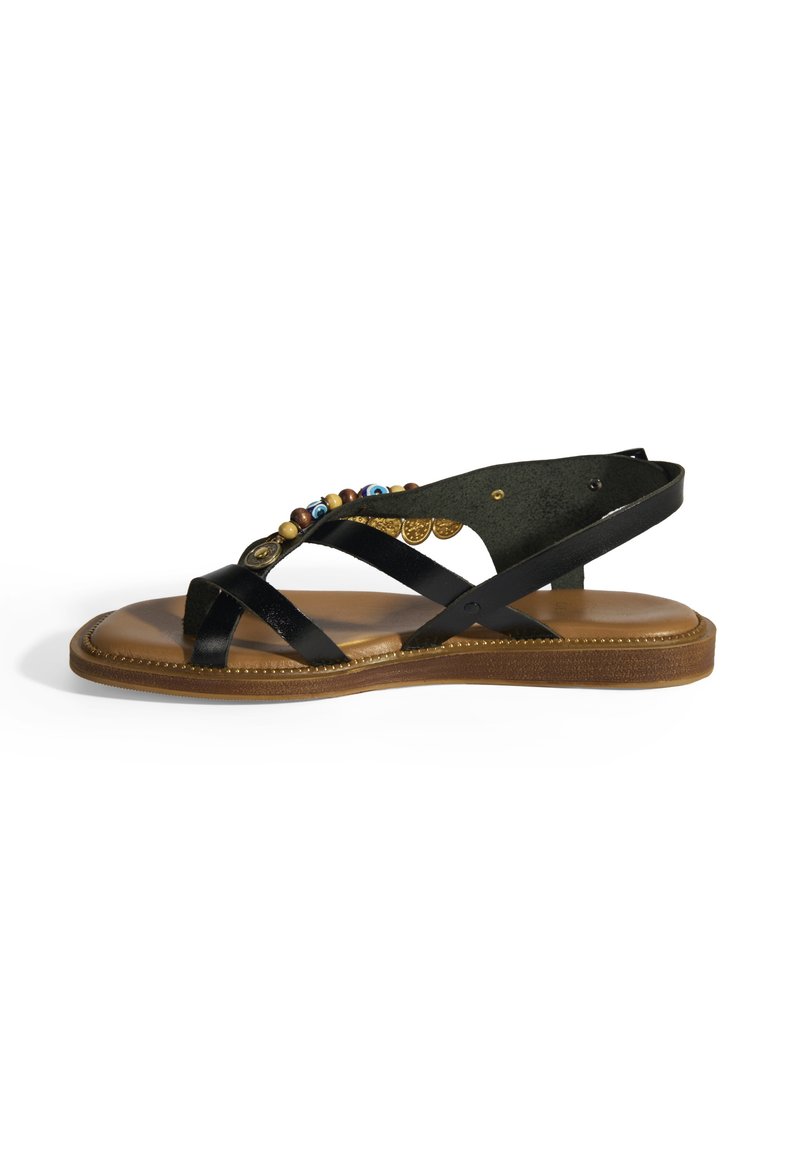Schwarze Leder-Sandale mit einem strukturierten Fußbett, verzierten Perlen und einem Kreuzband-Design. Flache Sohle mit einem braunen Grund und goldenen Akzenten.