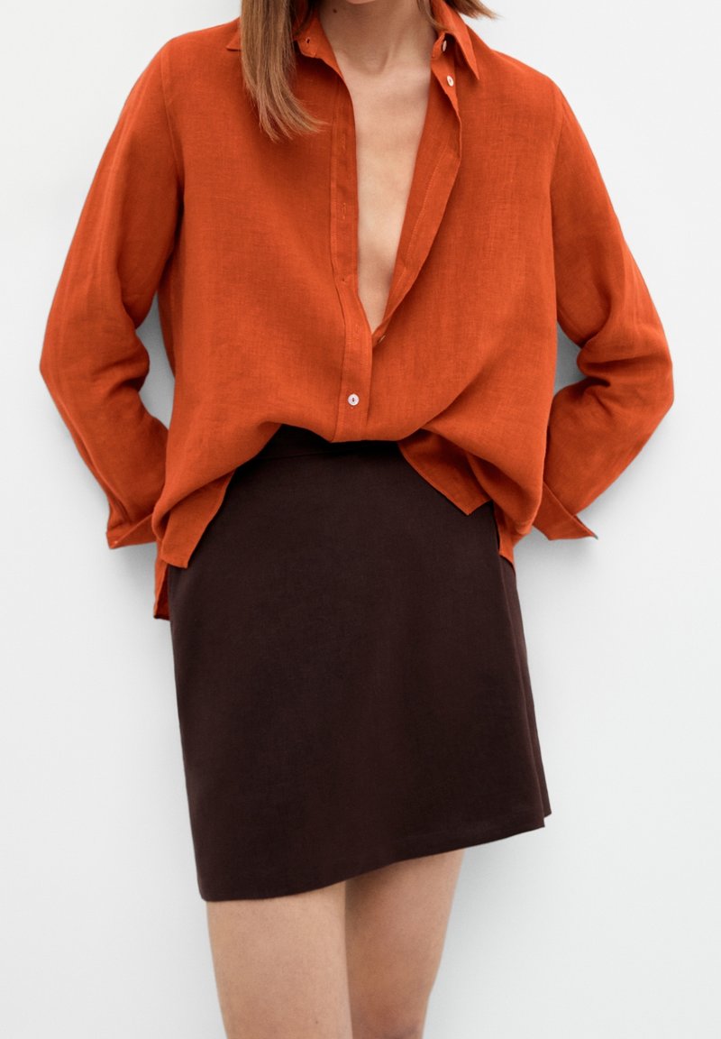 Chemise en lin couleur rouille avec un décolleté en V plongeant, associée à une jupe moulante marron foncé. Les deux vêtements ont une texture lisse.