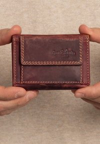 Brown leather wallet with visible stitching and a front flap, embossed with "Gusti Leder studio." Compact rectangular shape.