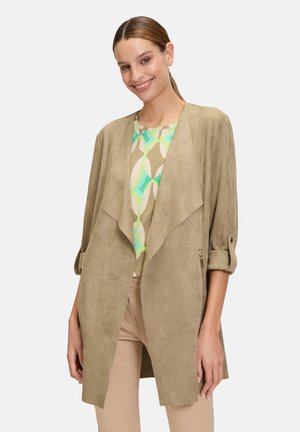 Veste en suédine beige avec une ouverture devant, des manches longues et deux poches zippées, superposée à un haut à motifs verts et beiges.