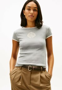 Szara bawełniana koszulka z krótkim rękawem, kontrastowym białym kołnierzykiem i beżowym logo "HILFIGER" na piersi. W zestawie z brązowymi spodniami plisowanymi.