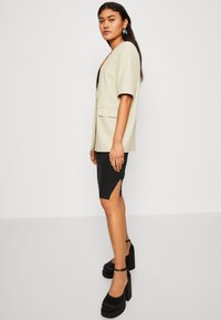 Ljusbeige kavaj med korta ärmar, som matchas med en svart ribbad kjol med en sidosprund. Svarta plattformsskor fulländar outfiten.