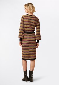 Abito in maglia con un motivo zigzag multicolore in rosso, giallo e nero. Presenta maniche a palloncino e una vita adatta, abbinato a stivali neri.