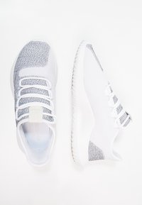 Vita atletiska skor med ett strukturerat grått stickat ovandel, elastiska snörning och en flexibel vit sula. Minimalistisk design och lätt vikt.