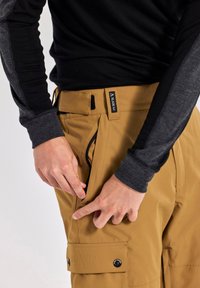 Khaki cargo pants met ritszakken, textuurstof en logodetail bij de tailleband. Gecombineerd met een zwart longsleeve shirt.