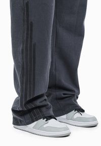 Donkergrijze joggingbroek met drie verticale strepen langs de zijkanten. Gecombineerd met witte sneakers met grijze accenten en zwarte veters.