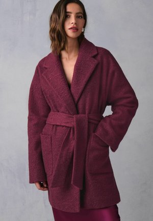 Burgundy, texturerad kappa med breda slag, ett bälte av sashes och två framfickor. Tyget är mjukt och ger ett mysigt intryck.