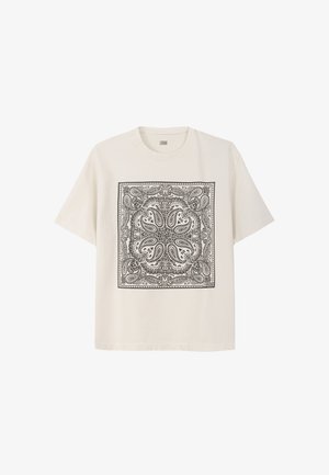 Bawełniany t-shirt w kolorze kremowym z czarnym wzorem paisley w formie kwadratu. Luźny krój, krótkie rękawy i okrągły dekolt.