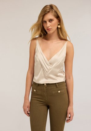 Camisola di raso crema con scollo a V profondo e design plissettato, abbinata a pantaloni alta vita verde oliva con dettagli di bottoni dorati.