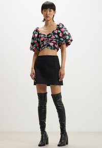 Top corto floreale con maniche a sbuffo nei colori verde, rosa e nero, abbinato a una mini gonna nera con dettaglio di bottoni e stivali neri alti fino alla coscia.