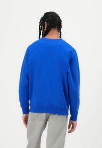 Blauwe sweatshirt met een ronde halslijn, ribgebreide manchetten en zoom. De stof lijkt zacht met een gladde textuur. Gemaakt in combinatie met lichtgrijze broek.