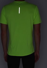 Camiseta deportiva de manga corta en color verde neón, con una textura de malla y una franja vertical reflectante en la parte posterior para mayor visibilidad.