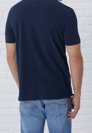 Mörkblå kortärmad t-shirt med rund hals, kombinerad med ljusblå jeans som har dekorativ sömnad på fickorna.