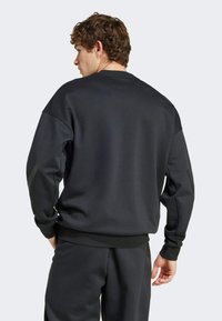 Sweatshirt noir à coupe ample, avec des poignets et un ourlet côtelés, un col rond et une texture douce. Fait partie d'une tenue assortie.