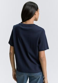 Tamsiai mėlyna, trumpų rankovių marškinėliai, pagaminti iš minkštos medžiagos. Turi apvalų iškirpimą ir laisvą siluetą. Atgalinis vaizdas rodo glotnią tekstūrą.