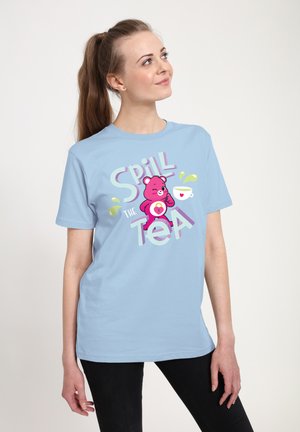 Lyseblå t-shirt med et pink bjørne-grafik og teksten "Spill the Tea" med legende sprøjt af grøn. Korte ærmer, rund halsudskæring.