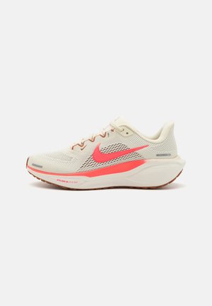 Zapatilla deportiva en malla crema con acentos y logo en rosa brillante. Presenta un diseño con cordones, cuello acolchado y suela de goma para tracción.