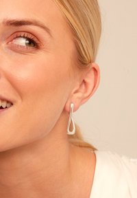 Pendientes de gota de plata con un diseño en forma de lazo. Textura suave y reflectante; forma alargada que complementa el lóbulo de la oreja.