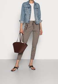 Veste en denim, t-shirt blanc, joggers marron texturés avec zips latéraux, et sac à main marron embossé façon croco. Sandales noires à talons complètent la tenue.