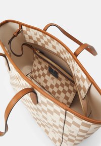 Béžová a hnědá kostkovaná taška s hnědými uchy, obsahující vnitřní zipovou kapsu se shodným vzorem a zlatým zipem.