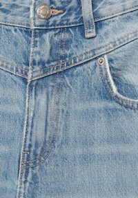 Világoskék farmernadrág közeli kép, amely fémgombot, övbútort, narancssárga varrást és az elülső zsebek részleteit mutatja.