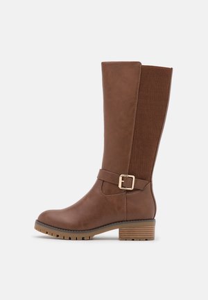 Botte mi-mollet marron avec un petit talon épais, une sangle à boucle latérale et un panneau élastique côtelé à l'arrière pour plus de flexibilité et un meilleur ajustement.