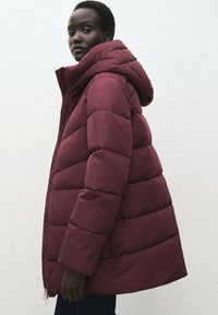 Chaqueta acolchada burdeos con una gran capucha, que presenta un diseño acolchado, un generoso relleno y una silueta esbelta y alargada.