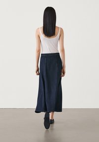 Denimmaxikjol i djupblått med rak silhuett, med ton-i-ton-sömmar och ett slätt midjeband. Bärs över en lätt linne-top.