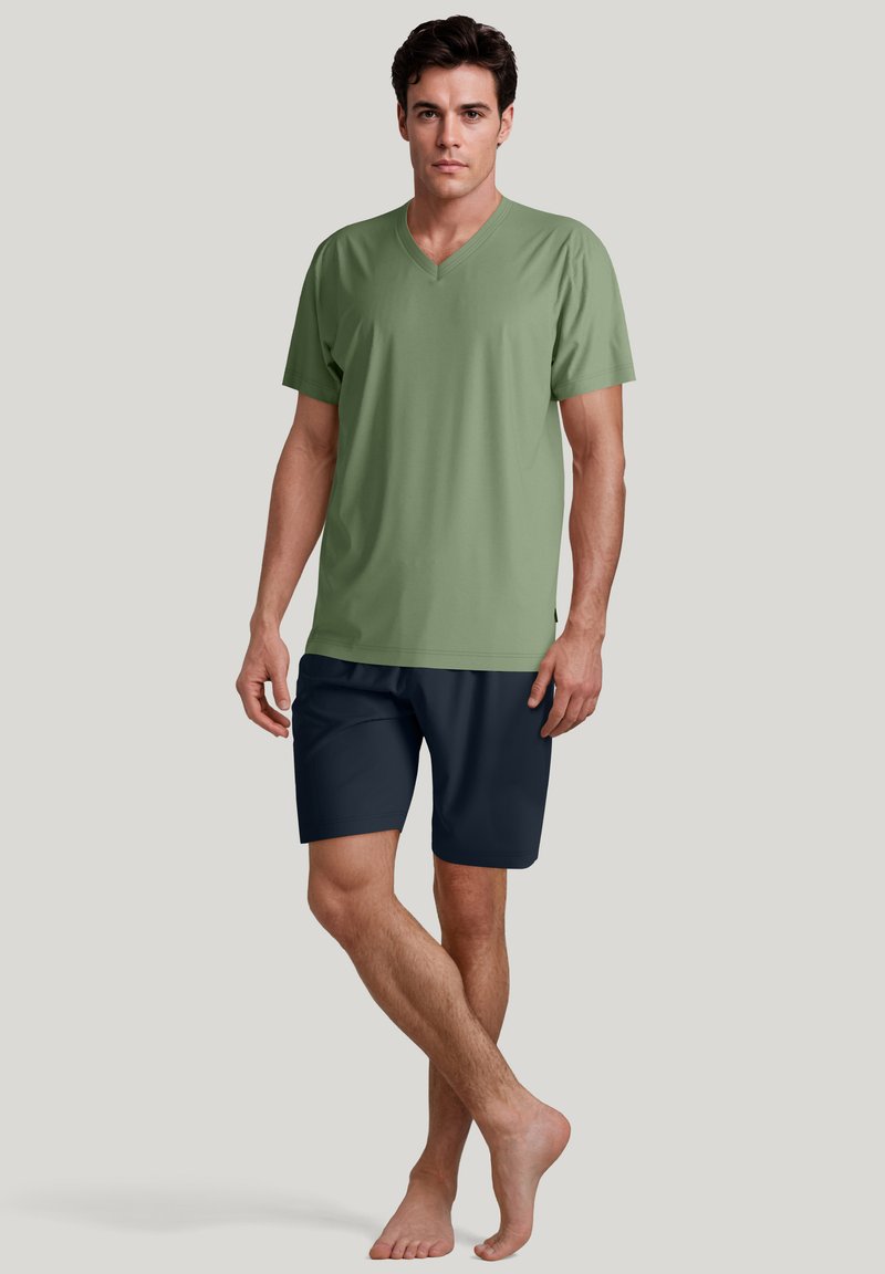 Groene V-hals T-shirt met korte mouwen, gecombineerd met marineblauwe shorts. De stof lijkt glad. Model staat blote voeten met één been iets gekruist.