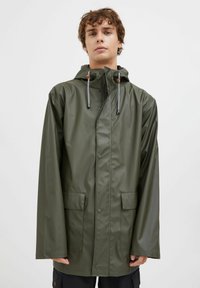 Jachetă impermeabilă de culoare verde măsliniu, cu glugă, închidere frontală cu snaps și buzunare laterale. Textură netedă și șnururi ajustabile la gât.