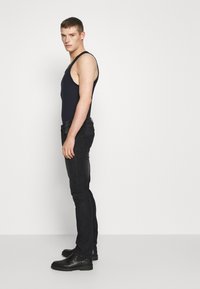 Top de tirantes de color marino, jeans negros ajustados y botas de tobillo negras. Contraste entre la tela transparente del top y la textura de mezclilla de los jeans.