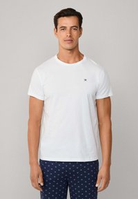 Bílý bavlněný tričko s kulatým výstřihem a krátk�ými rukávy, se malým námořnickým logem na hrudi. V kombinaci s námořnickými kalhotami se vzorem.