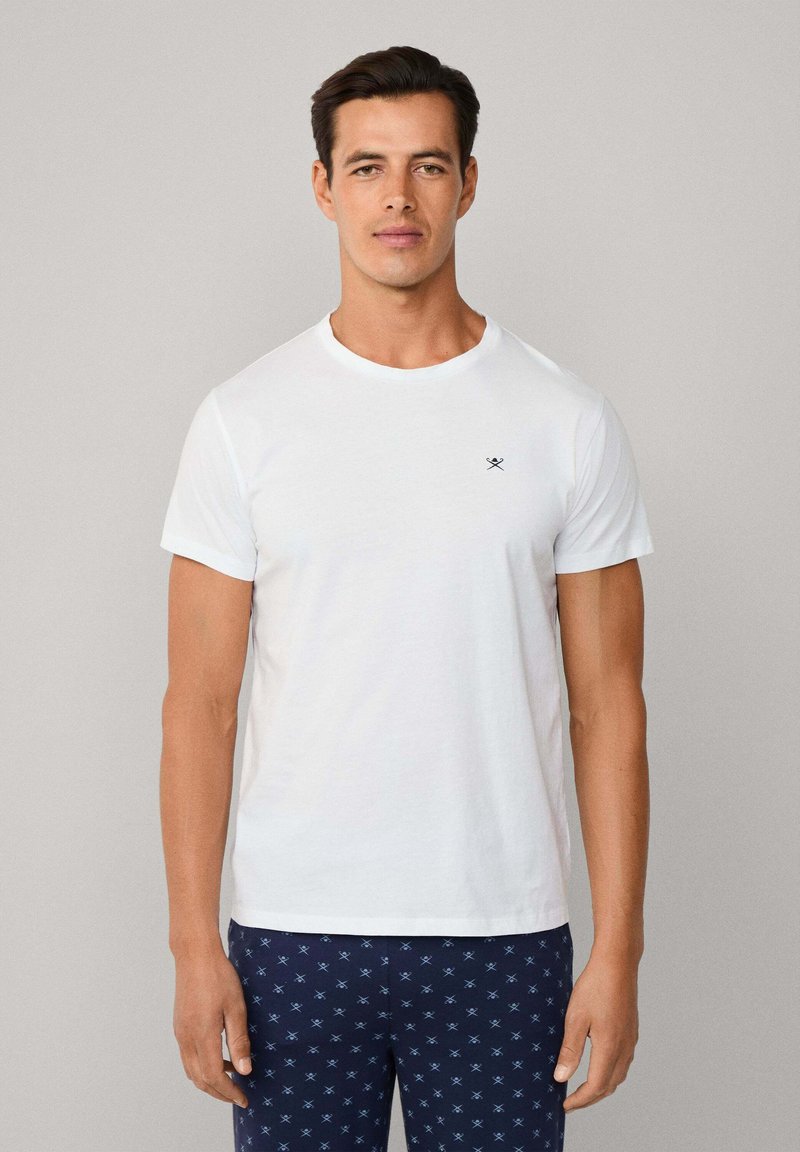 Bílý bavlněný tričko s kulatým výstřihem a krátkými rukávy, se malým námořnickým logem na hrudi. V kombinaci s námořnickými kalhotami se vzorem.