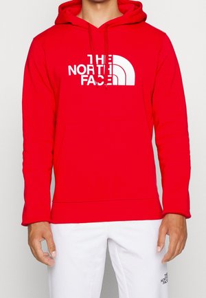 Czerwona bluza z kapturem wykonana z miękkiego materiału z dużym białym logo przedstawiającym półksiężyc na piersi. Posiada przednią kieszeń i kaptur ze sznurkiem.