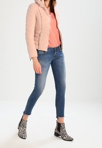 Jasnoróżowa pikowana kurtka z kapturem, pomarańczowa bluzka, niebieskie obcisłe dżinsy i czarno-białe botki w panterkę z elastycznymi bocznymi panelami.