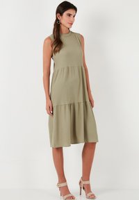 Sleeveless midi dress in olive green, featuring a fitted bodice and a tiered bottom. Made from ribbed fabric with a smooth texture.