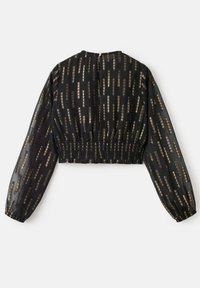 Avskuren svart blus med långa, genomskinliga ärmar. Har ett guldmönster av vertikala linjer. Elastisk midja bak med knäppning.